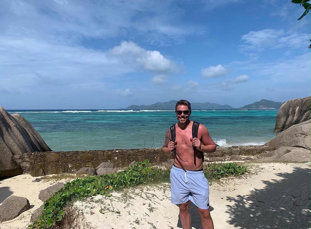 Kaká na praia em Seychelles, com mar azul e rochas ao fundo