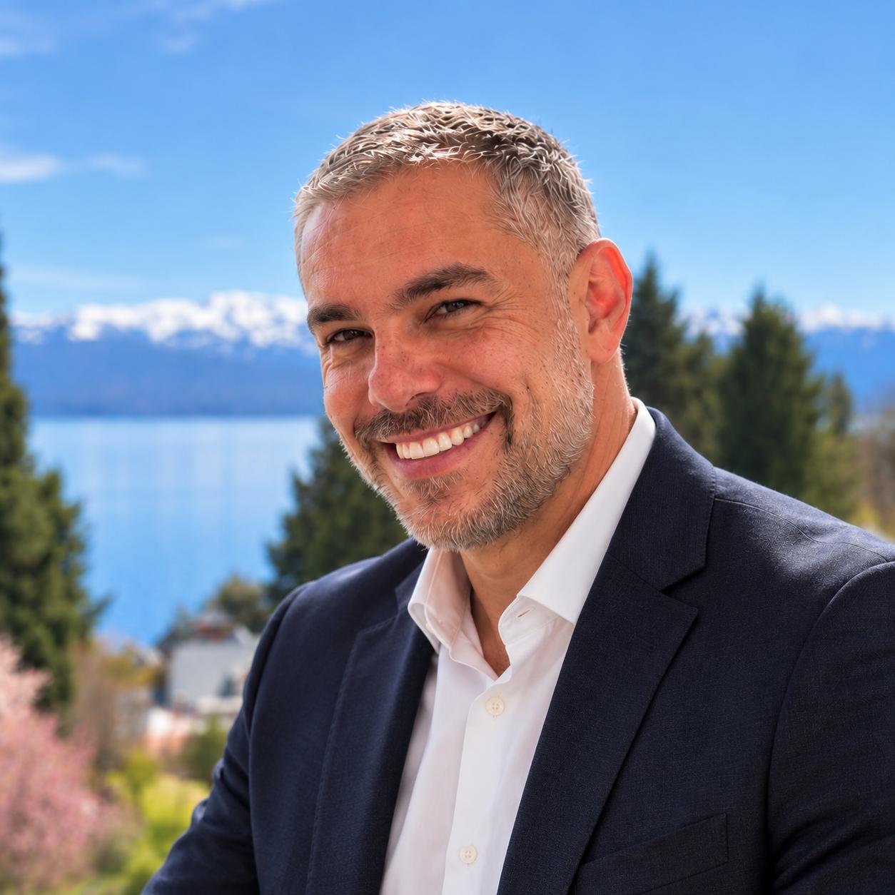 Carlos Eduardo Guimarães, o Kaká da KS Turismo, sorrindo de terno, com lago e montanhas ao fundo